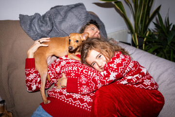 Family wearing Christmas sweaters relaxing on sofa with their dog