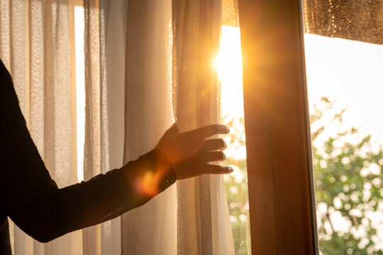 Fototapeta woman's hand She opened the curtains on the window. There was morning light through the window in her room, looking at the view of the mountains and trees as the sun rose  