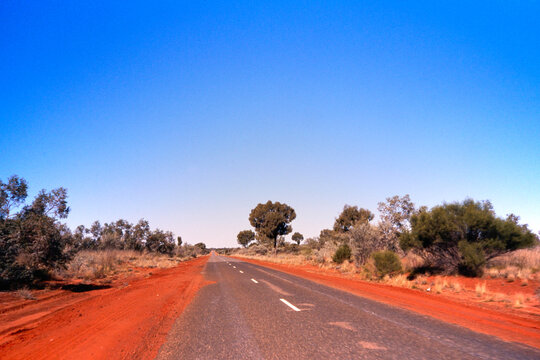 Open red dirt road stretches through arid landscape of Aussie outback 