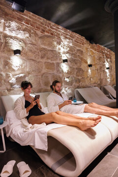 ?ouple lying on comfortable loungers and using phones at spa club