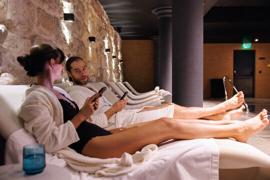 ?ouple with cellphones looking at each other on loungers at spa club