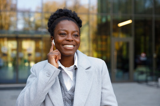 Happy broker putting earphone in ear standing in front of office 