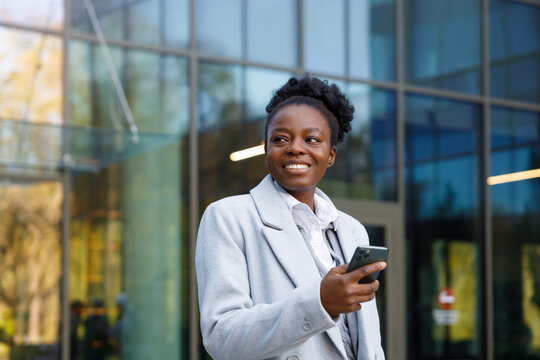 Smiling crypto trader standing with smartphone in hand near office