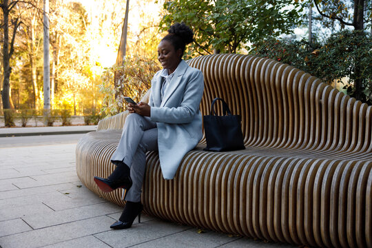 Self employed woman sitting on bench in park with mobile phone in hand