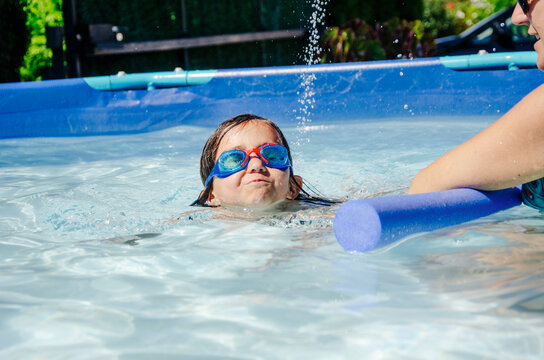 Girl learning to swim with swimming goggles and a blue tube in pool