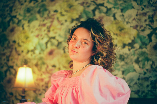Smiling woman posing in pink dress in vintage bedroom