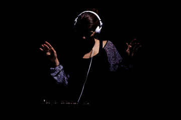 Female DJ with headphones on a mixer. Girl playing techno music against black background.