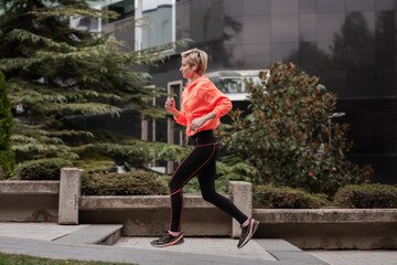 A dynamic photo featuring a young woman jogging in a city setting, wearing a bright orange jacket...