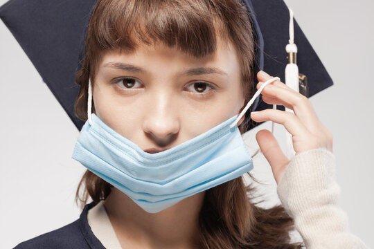 Graduation girl wearing gown and cap. Female student putting on protective face mask.
