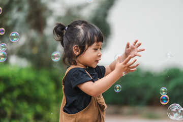 toddler girl playing soap bubble in park