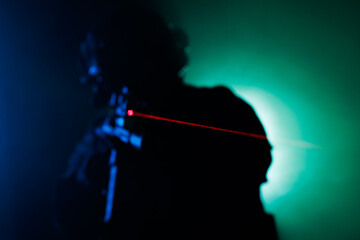 Fototapeta premium Silhouette of Person Aiming with Laser Sight Amid Dramatic Background