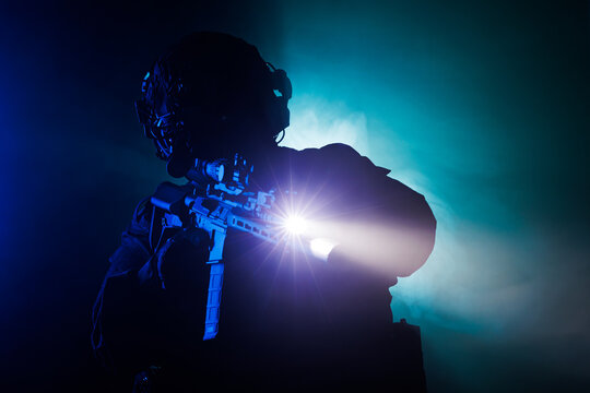 Silhouette of armed tactical person with flashlight and rifle in low light setting