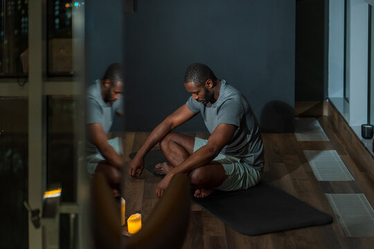 Man Sitting on Yoga Mat in Candlelit Room