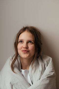 Teenager wrapped in blanket sitting indoors at home