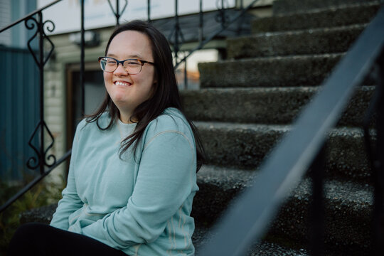 Smiling Individual Sitting on Outdoor Steps Wearing Casual Shirt.