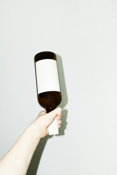 Hand holding glass wine bottle with etiquette & hard direct flash