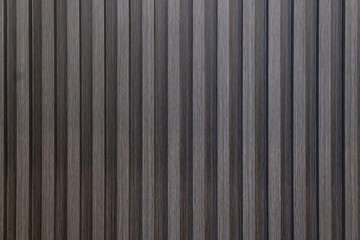 Close-up texture of dark wood wall paneling. Features vertical wooden slats creating a rhythmic pattern with visible grain. Ideal backdrop or surface detail