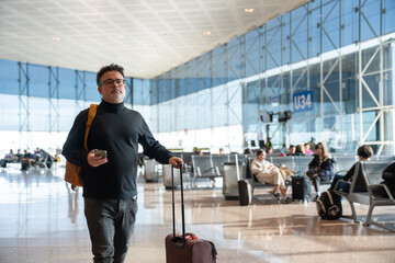 Man walking in airport holding phone and suitcase