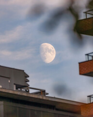 Waxing near full moon seen rising above apartment buildings in a hazy blue sky.  Toronto Ontario