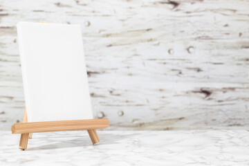Vertical blank canvas on an easel on a marble table in front of a wooden background. Minimalist concept for art or design