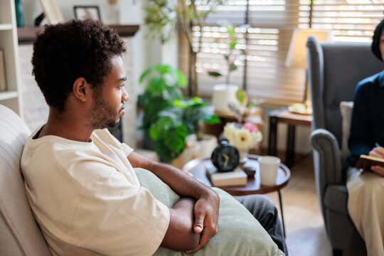 Insecure young man sitting with pillow during therapy session