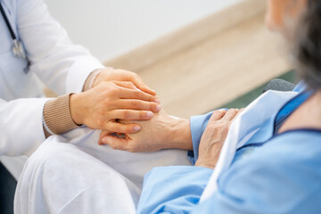 Doctor comforting senior patient by holding hands, providing care
