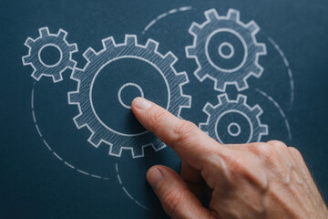 Hand points to mechanical gear drawings on chalkboard symbolizing consulting and teamwork in engineering and technical problem solving