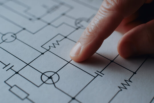 Finger points to mechanical circuit diagram on paper highlighting consulting work in engineering and technical design for electrical projects