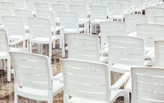 Rows of white plastic chairs arranged on a concrete surface