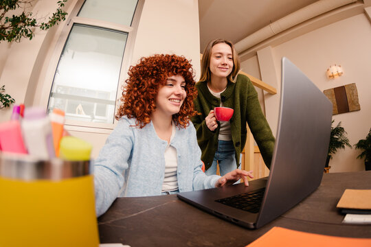 Wide shot of co-workers chatting while solving work tasks on a laptop