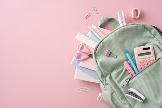 Green backpack filled with school supplies including a calculator, notebooks, and stationery on a pink surface