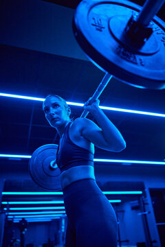 Strong individual lifting weights in a blue-lit gym