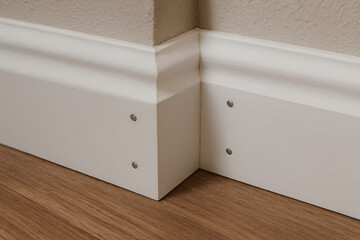 Detailed close up of white baseboard with corner joint on wooden floor