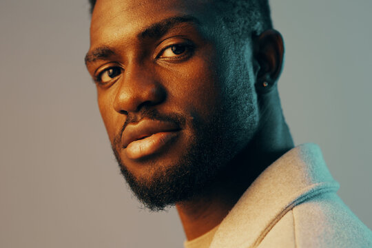 Close up portrait of a young Black man with a stylish haircut, dressed in a light sweater, expressing confidence against a softly lit background with warm tones