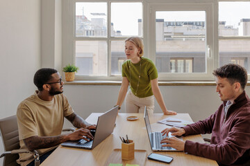 Marketing team working on laptops in modern office with big window