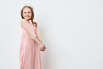 Smiling girl in a pink dress with sheer sleeves, posing against a simple white background, evoking...