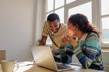 Coworkers smiling and collaborating on laptop in modern office