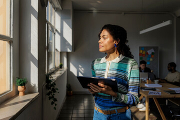 Thoughtful manager holding tablet looking out office