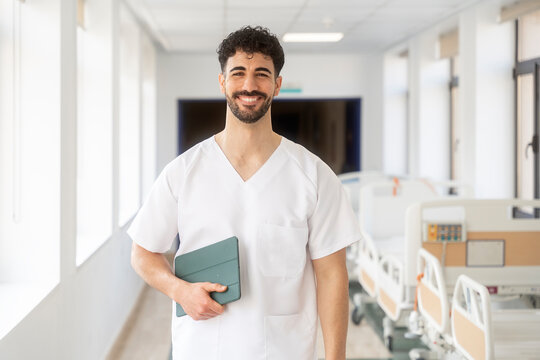 Smiling doctor holding tablet walking in hospital corridor