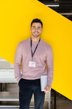 Professional man with lanyard smiling against yellow background