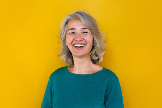 Mature chinese woman smiling against a vibrant yellow background