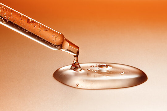 Glass pipette with anti-age moisturizing face serum on orange backdrop