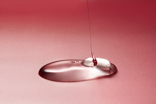 Clear liquid dripping on smooth gradient pink background.