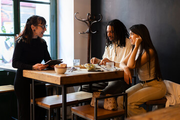 Wedding planner discussing menu options to young couple in restaurant