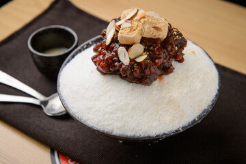 Shaved ice with milk ice, red beans, rice cake covered in soybean powder, and topped with almond slices
