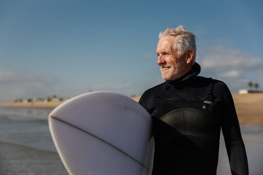 Active Senior Man Carrying Surfboard on a Sunny Day at the Beach