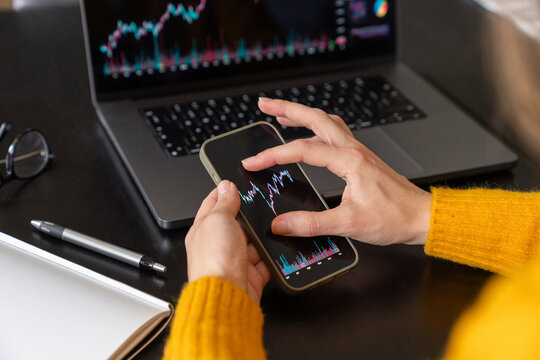 Investor analyzing stock graph using phone and laptop