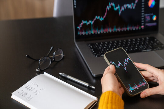 Person analyzing stock chart using phone and computer