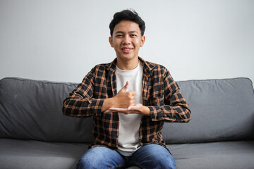 Smiling teenage boy with hearing disability showing thumb up on palm as a sign language