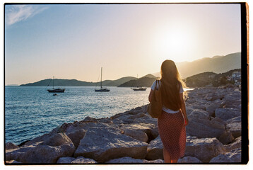 Anonymous woman standing at the seashore watching yachts passing by